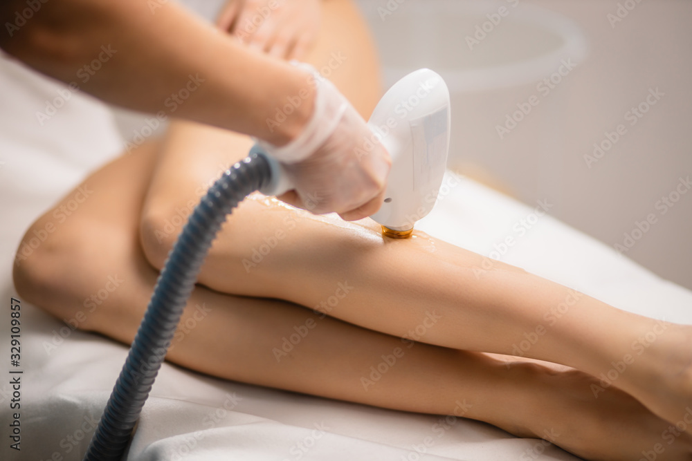 Naklejka premium young slender woman get hair removal procedure on legs. beauty cosmetic procedures in salon. beautiful woman has prefect smooth and soft skin on legs