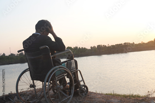 Young disabled man with field background.He is wearing a hat and sitting on wheelchair.He is looking into river.despair,lonely,hope.Photo concept depression and Patient.