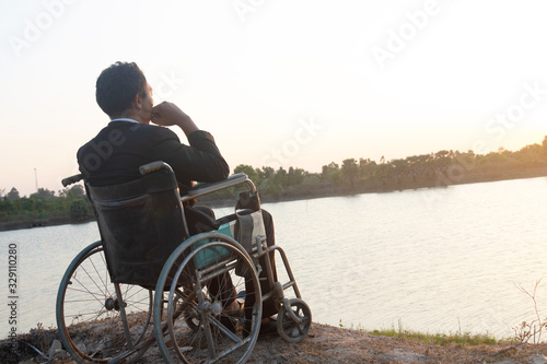 Young disabled man with field background.He is wearing a hat and sitting on wheelchair.He is looking into river.despair,lonely,hope.Photo concept depression and Patient.