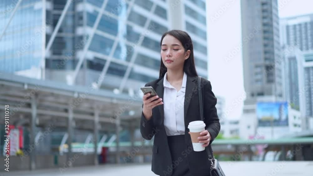Slow Motion shot of Asian business woman holding hot coffee and reading text massage on mobile phone while walking in the urban town Slow Motion shot of Asian business woman holding hot coffee and reading text massage on mobile phone while walking in the urban town