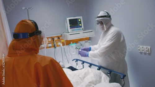 Doctor in an Orange Protective Suit Enters Isolation Room with Coronavirus Patients - Handheld Shot