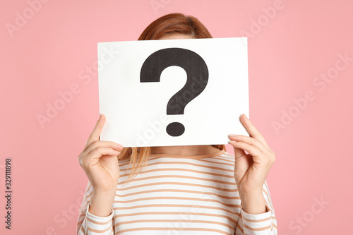 Woman holding question mark sign on pink background photo