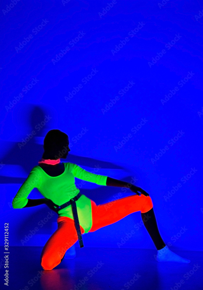 real shot under black light,  young woman in dark under ultraviolet light wearing UV 80's style fashion. Glowing neon effect on blue background. Soft selective focus