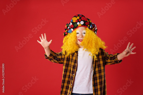 Funny little boy in clown costume on red background. April fool's day