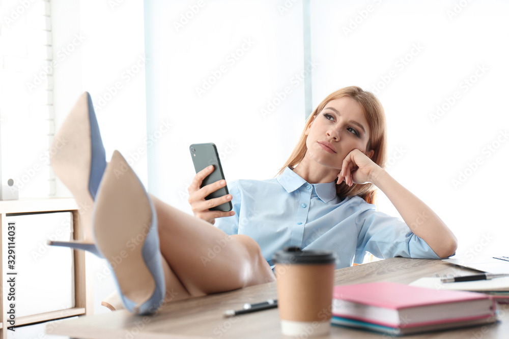Lazy employee using smartphone while resting at table in office Lazy employee using smartphone while resting at table in office