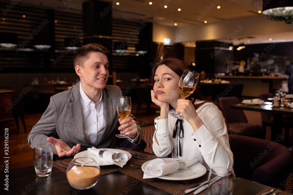 bored caucasian woman with champagne and handsome man entertaining her. male in love with her, while woman is not interested in rendezvous with him. in luxury restaurant