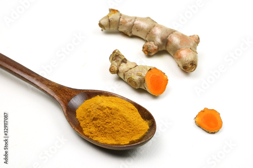 Turmeric powder in a wooden spoon and fresh turmeric roots isolated on a white background is an ingredient in turmeric foods and ingredients in skin care products. Turmeric helps strengthen the skin.
