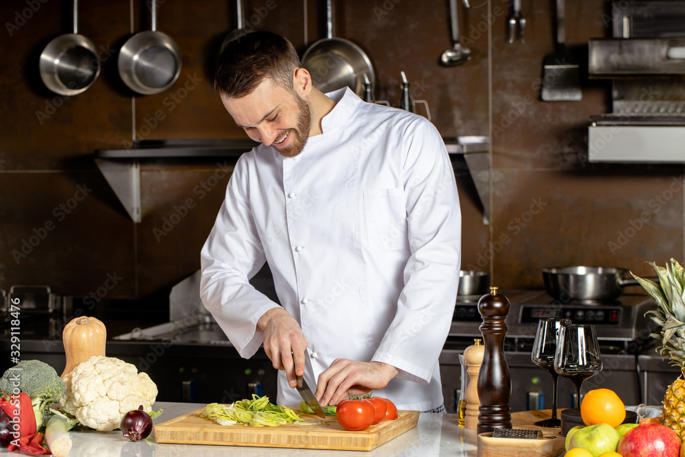 young caucasian chef-cook cut vegetables in kitchen. cook make vegetarian dish for restaurant visitors, man in white apron use sharp knife for better cutting young caucasian chef-cook cut vegetables in kitchen. cook make vegetarian dish for restaurant visitors, man in white apron use sharp knife for better cutting