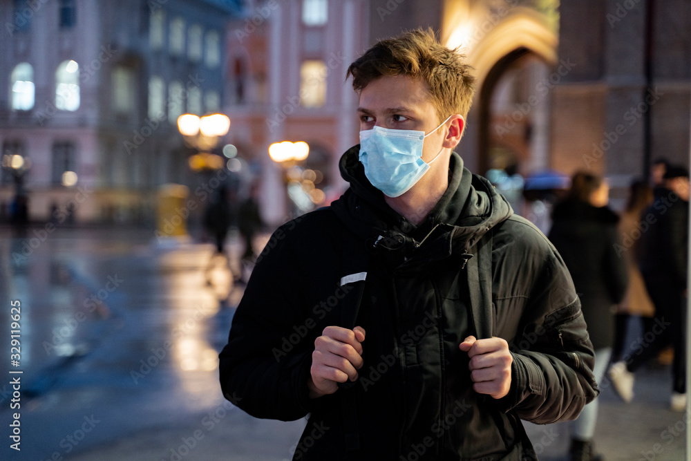 Worried teenager in the city at night wearing surgical mask over his face Worried teenager in the city at night wearing surgical mask over his face