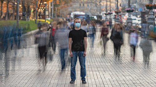 The man with medical face mask stands on the crowded urban street