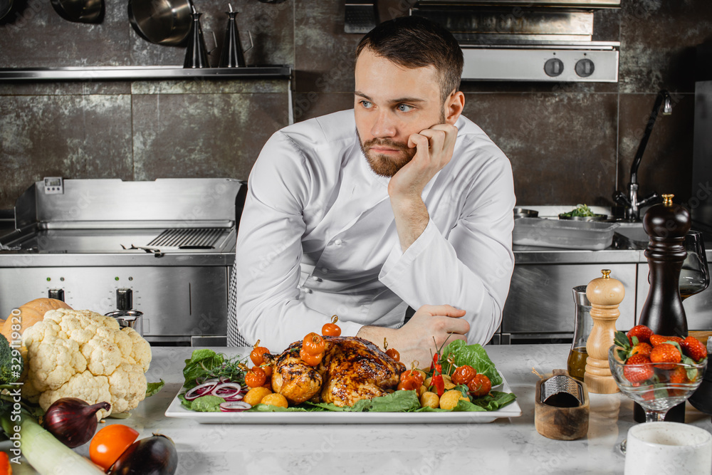 thoughtful caucasian chef-cook in kitchen, man leaned on table and think, look side. cooked meat on table. cooking, fun, culinary concept