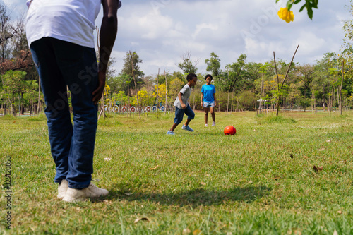 African American family with son and daughter plays soccer together on green field for relaxation - Family Bonding Recreation Sports Football Concept