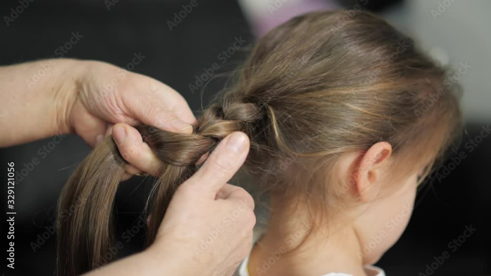 grandmother combs her granddaughter's hair, braid the ponytail grandmother combs her granddaughter's hair, braid the ponytail