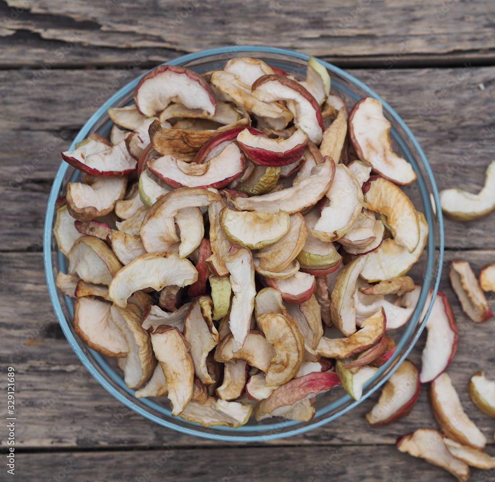 Background of dried homemade fruit Apple chips or slices in a glass plate on a wooden table. Health benefits of dried fruits, vegetarian food. Background of dried homemade fruit Apple chips or slices in a glass plate on a wooden table. Health benefits of dried fruits, vegetarian food.