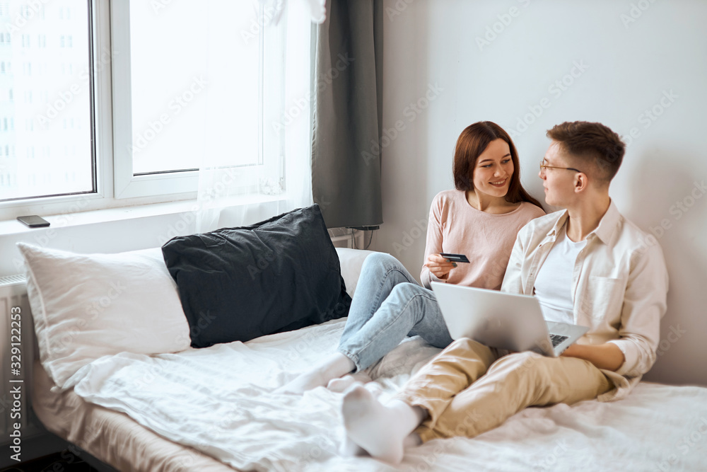 young happy people sitting on the bed, enjoying shopping online, Online payment, full length side view photo