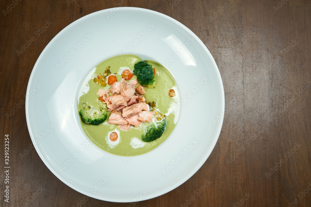 Appetizing and healthy green pea cream soup with broccoli and salmon cooked in a smoker on a wooden background. Top view Appetizing and healthy green pea cream soup with broccoli and salmon cooked in a smoker on a wooden background. Top view