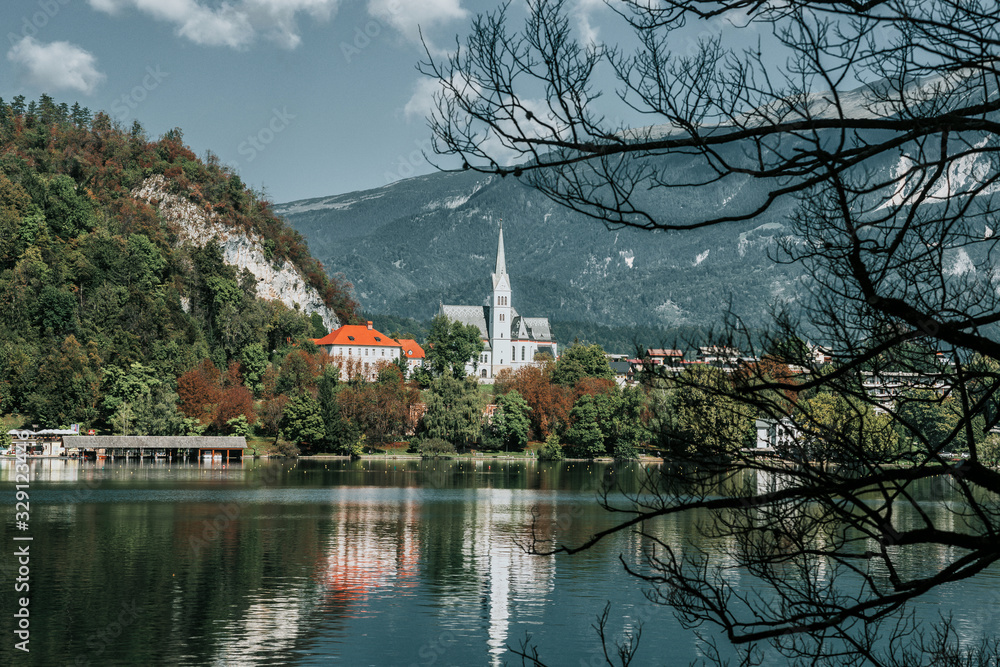 Bled, Slovenia. Lake Bled and a view of the historic cathedral near the shore through a frame of tree branches. Rest in summer or autumn on a mountain lake in Europe. A popular tourist destination.