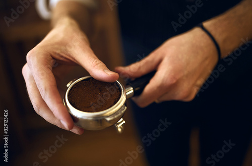 coffee shop owner holding a portafilter containing freshly ground coffee, close up side view photo, blurred background.necessary component that is part of every espresso machine