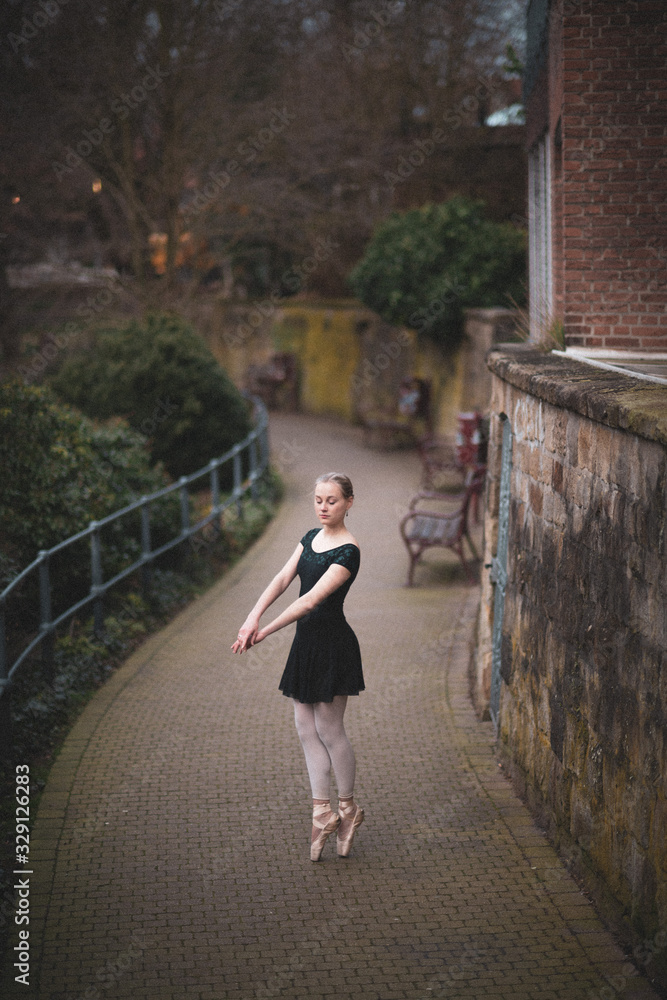 Healthy young beautiful blonde girl with a black dress - Ballerina - dancing Ballet in the middle of a lonely old street with bushes, trees and nature around her in a very peaceful atmosphear. Healthy young beautiful blonde girl with a black dress - Ballerina - dancing Ballet in the middle of a lonely old street with bushes, trees and nature around her in a very peaceful atmosphear.