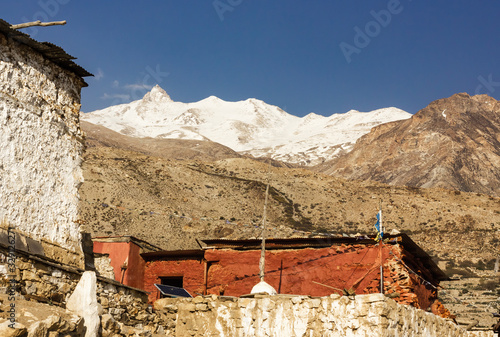 The ancient Buddhist monastery with red in the village of Nako with a snow covered Himalayan peak in the background in Kinnaur, India.