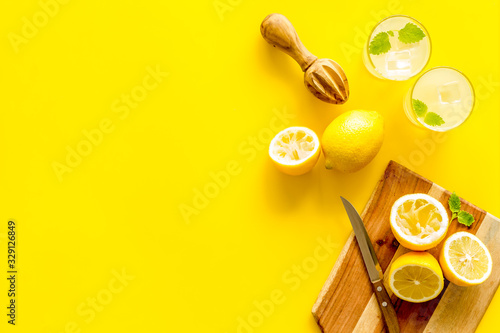 Homemade lemonade in glasses near juicer and cut lemons on yellow background top-down copy space