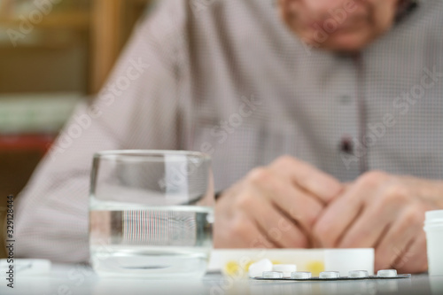 pills and glass of clear water near elderly man on table