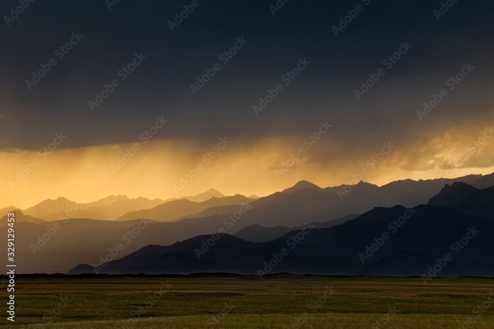 Kyrgyzstan. The sun rays at sunset break through the gloomy rainy clouds