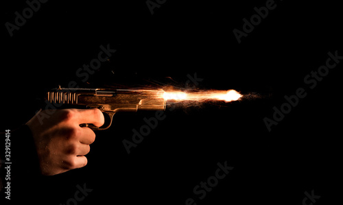 The hand presses the trigger of the gun and the flame from the shot escapes from its muzzle