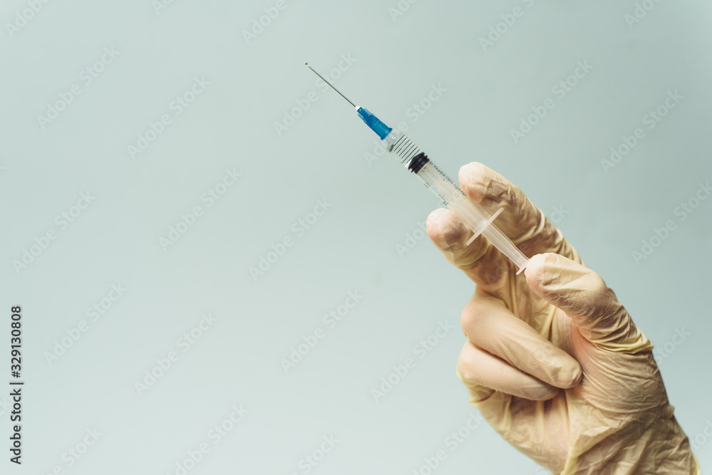 Doctor's hand in a white rubber glove holds a medical syringe on a blue background. The concept of medicine and medical care for the patient Doctor's hand in a white rubber glove holds a medical syringe on a blue background. The concept of medicine and medical care for the patient