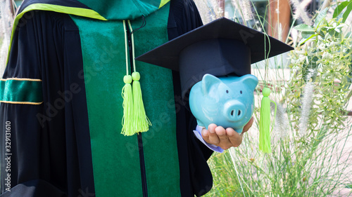 Piggy bank is holden by a person in graduated uniform. saving money for education, future investment concept photo