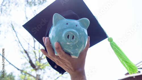 Piggy bank is holden by a person in graduated uniform. saving money for education, future investment concept photo