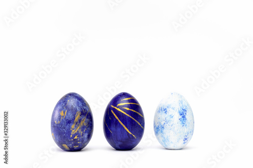 Three easter eggs trendy colored classic blue, white and golden decorated on white table. Happy Easter card with copy space for text. Minimal style.