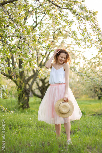 Young attractive woman with curly hair walking in a green flowered garden. Spring mood photo