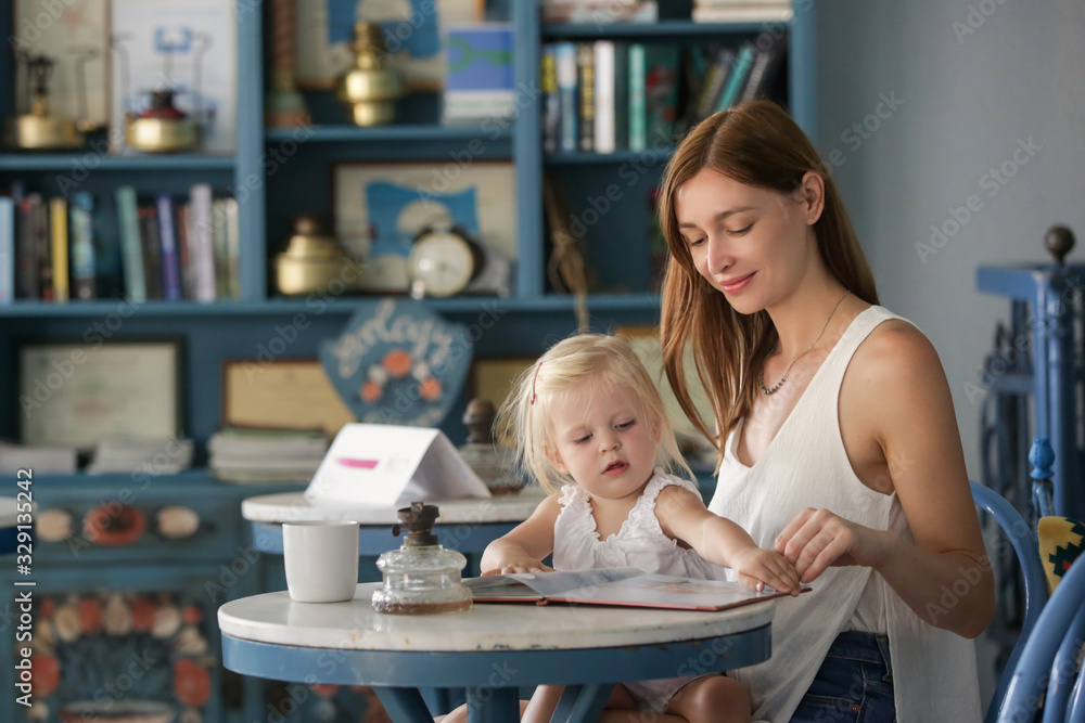 Mother reading book to her daughter in cafe. Reading books aloud to children stimulates imagination and expands their understanding of the world. It helps them develop language and listening skills. Mother reading book to her daughter in cafe. Reading books aloud to children stimulates imagination and expands their understanding of the world. It helps them develop language and listening skills.