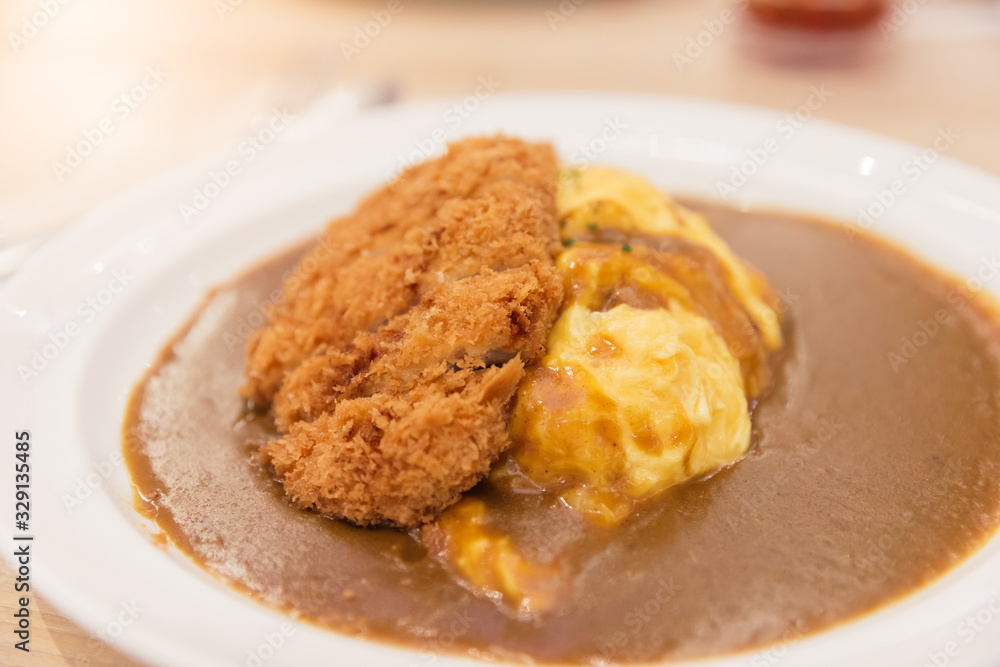 Japanese curry rice with omelet or omurice and deep fried breaded pork cutlet or Tonkatsu on wooden table Japanese curry rice with omelet or omurice and deep fried breaded pork cutlet or Tonkatsu on wooden table
