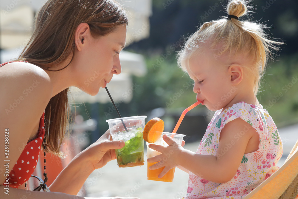 Fototapeta premium Mommy and her toddler girl enjoying a hot summer day at the beach bar, family vacation concept