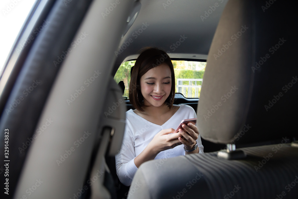 Asian teenager woman using a smartphone in back seat of car, Passengers use an app to order a ride and Peer-to-peer ride sharing concept