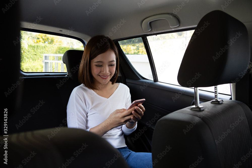 Asian teenager woman using a smartphone in back seat of car, Passengers use an app to order a ride and Peer-to-peer ride sharing concept Asian teenager woman using a smartphone in back seat of car, Passengers use an app to order a ride and Peer-to-peer ride sharing concept