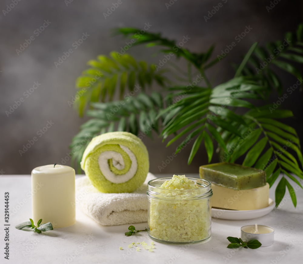 spa product composition with sea salt, solid soap, candles and bath towels on a background of green palm leaves. Spa Wellness Relax concept. place for text.