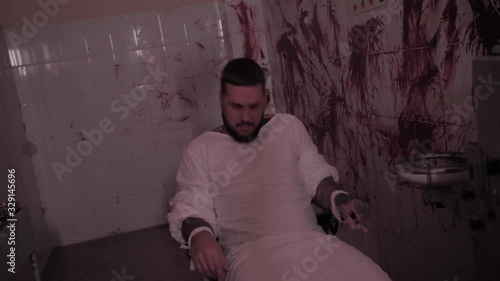 Crazy man in straitjacket tied to a chair, killer psychopath in a room with bloodied walls overdose photo