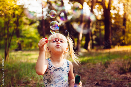 Canvas-taulu Funny little girl blowing soap bubbles in summer