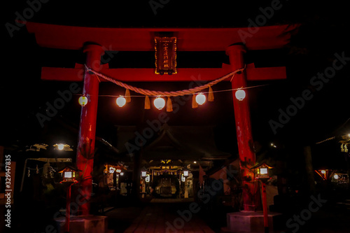 An orange torii gate leading to Mizukami Shrine lighted up at night in small Japanese city, Fujiyoshida. Torii gate is decorated with few lanterns, shining bright with light. Holly site.