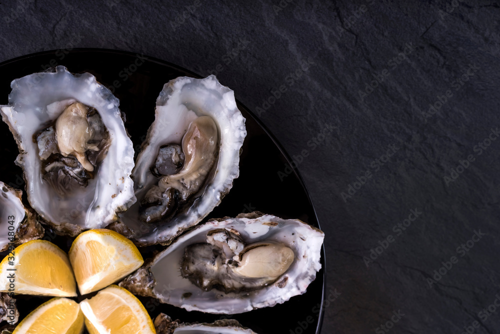 Oysters plate with lemon on grey background. Served table with oysters and lemon. Fresh oysters close-up top view. Healthy sea food. Oyster dinner with champagne in restaurant. Gourmet food. Sea food. Oysters plate with lemon on grey background. Served table with oysters and lemon. Fresh oysters close-up top view. Healthy sea food. Oyster dinner with champagne in restaurant. Gourmet food. Sea food.