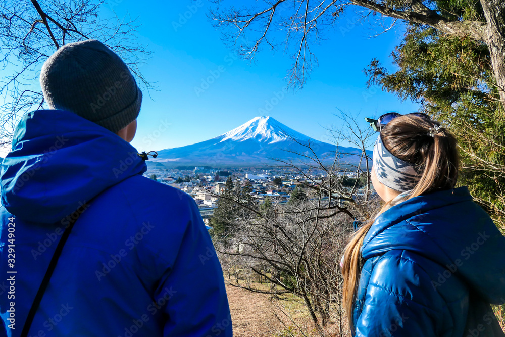 A couple standing on the hilltop above Chureito Pagoda, Japan and admiring Mt Fuji in front of them. They are holding hands, enjoying beautiful landscape. Holly mountain. Clear and sunny day. Love