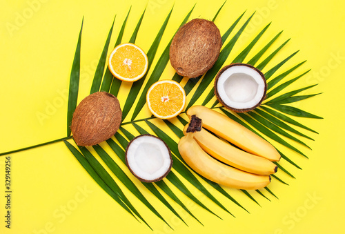 Summer tropical composition. Green tropical leaves of palm trees and monstera, coconut, orange, bananas on bright yellow background. Flat lay, top view, copy space. Creative background food, fruit