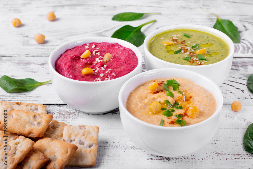 Colorful hummus in the white bowls on the white wooden table. Classic, beetroot and spinach chickpea dips Colorful hummus in the white bowls on the white wooden table. Classic, beetroot and spinach chickpea dips