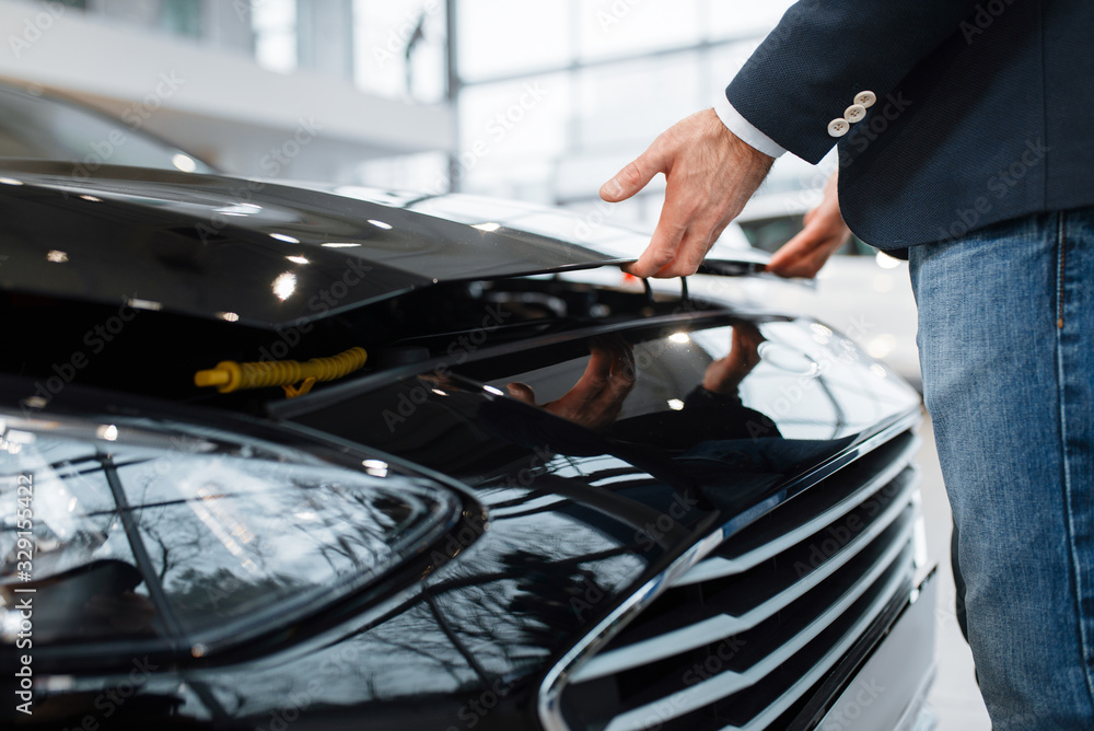 Man opens hood of transport in car dealership Man opens hood of transport in car dealership