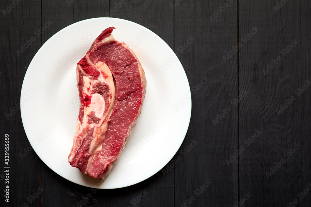 Raw veal steak on a white plate on a black wooden background. Raw veal steak on a white plate on a black wooden background.