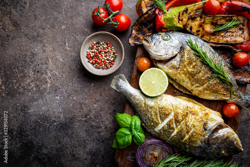 Baked Dorado fish, sea bream with grilled vegetables, herbs and seasonings, top view photo