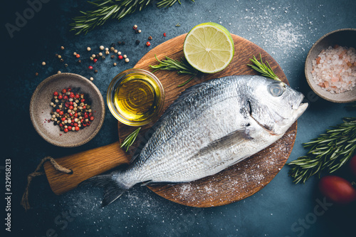Fresh ready to cook raw bream fish dorado with ingredients and seasonings like rosemary, salt, pepper, lime and olive oil, top view